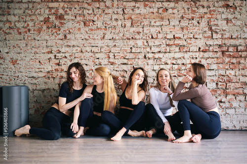 Cheerful women in activewear sitting near brick wall, yoga mats, ready start fitness training and rejoice at meeting. The concept of sports lifestyle and like-minded people. Yoga concept