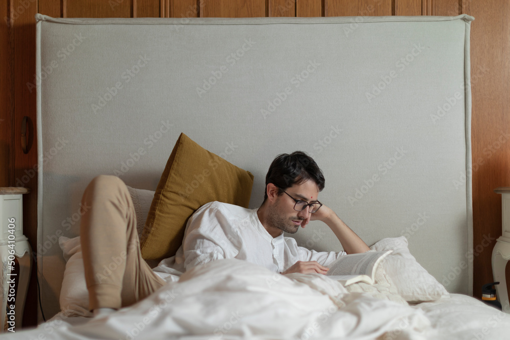 Man lies in bed while reading a book, nourishing his intellect and enjoying a pleasant leisure time at home. Man lies in bed while reading a book, nourishing his intellect and enjoying a pleasant leisure time at home.