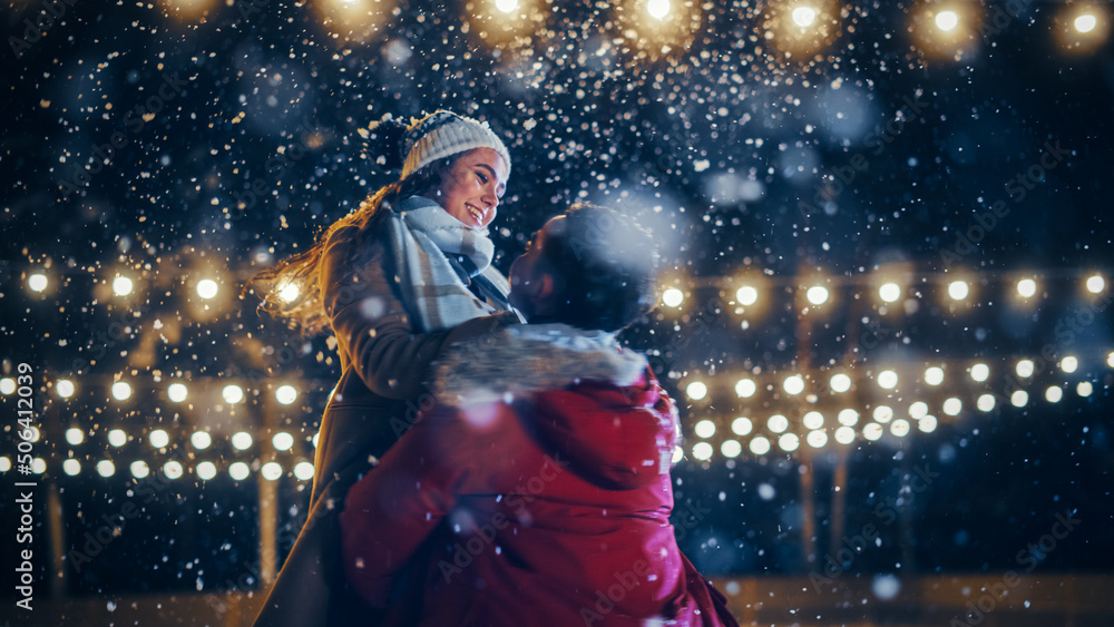 Naklejka premium Romantic Winter Snowy Evening: Ice Skating Couple Meeton on Ice Rink and Have Fun. Pair Skating Boyfrined Lifts His Beautiful Girlfriend and Spins. Love, Dance, Embrace, Figure Skate. Wide Shot