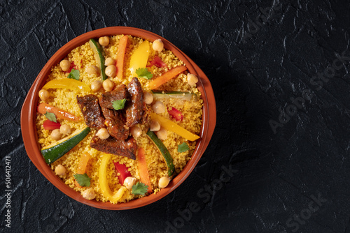 Couscous with meat and vegetables, festive Moroccan dinner, overhead shot with a place for text, on a black slate background