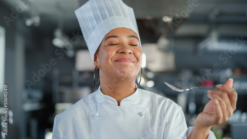 Obraz na plátně Restaurant Kitchen: Portrait of Black Female Chef Preparing Dish, Tasting Food and Enjoying it