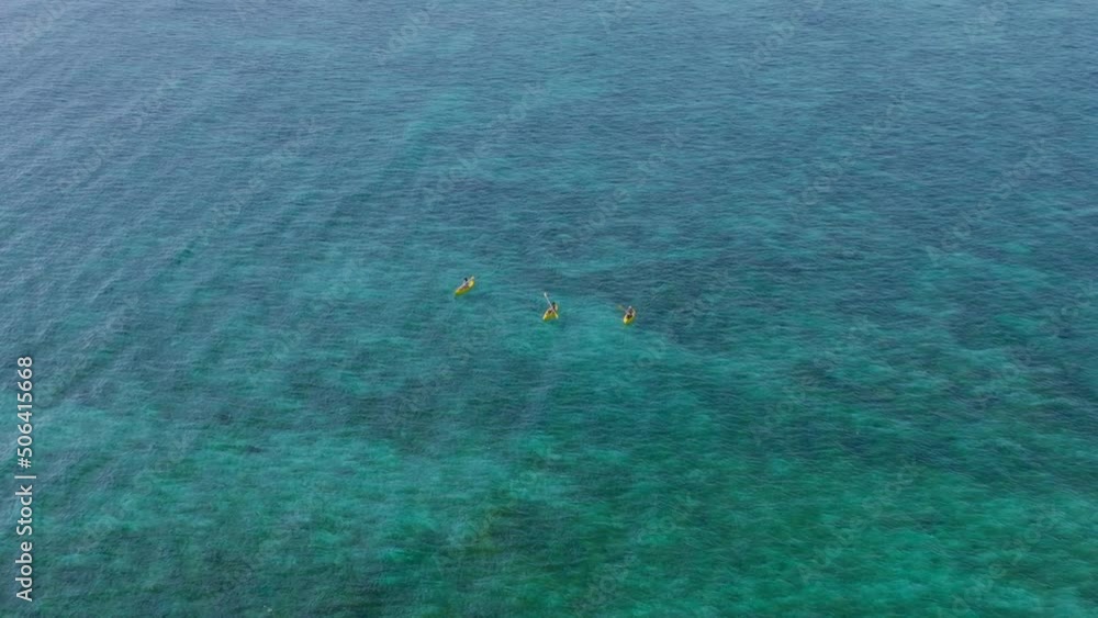 Three people in yellow kayaks paddling in shallow blue tropical water, aerial Three people in yellow kayaks paddling in shallow blue tropical water, aerial