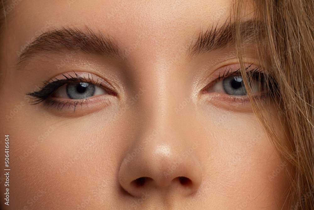 Obraz premium Close-up of woman's eyes with evening make-up. Fashionable shades of eye shadow, extremely long eyelashes and thick smooth eyebrows. Open beautiful look. Clean skin and white flowers