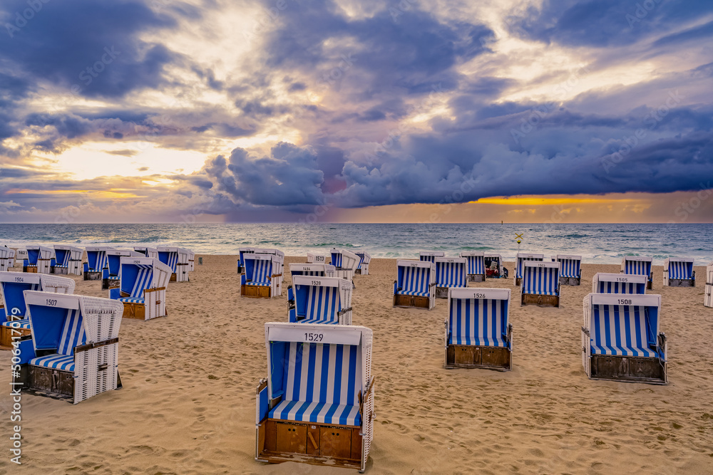 Roofed wicker beach chairs on sunset at the North Sea coast on Sylt, Germany
