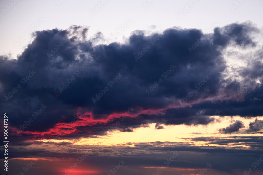 A large rain cloud with a reflection of light from the red sun at sunrise