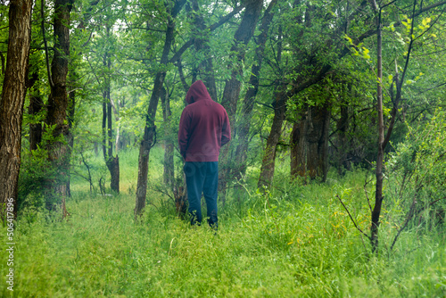 Obraz na plátně Unrecognized man in hoody peeing near tree in forest