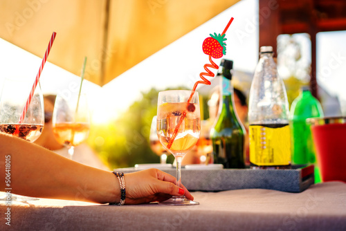 glass of alcoholic drink or soft drink at social gathering on sunny summer table, hand view