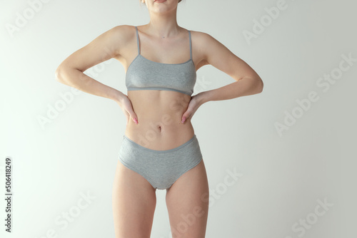 Cropped portrait of slim female body in cotton underwear posing isolated over grey studio background