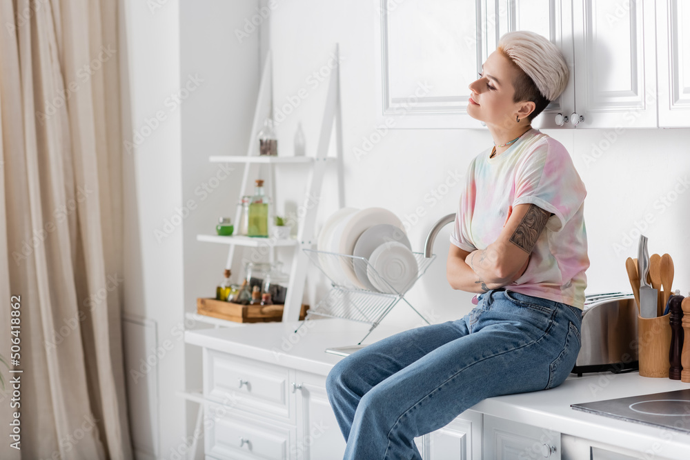 dreamy and smiling woman sitting on kitchen worktop with crossed arms and looking away dreamy and smiling woman sitting on kitchen worktop with crossed arms and looking away