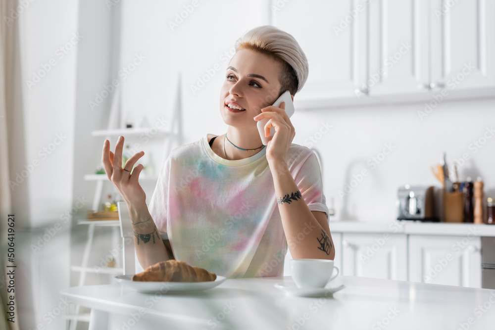 tattooed woman gesturing and talking on smartphone near croissant and coffee cup tattooed woman gesturing and talking on smartphone near croissant and coffee cup