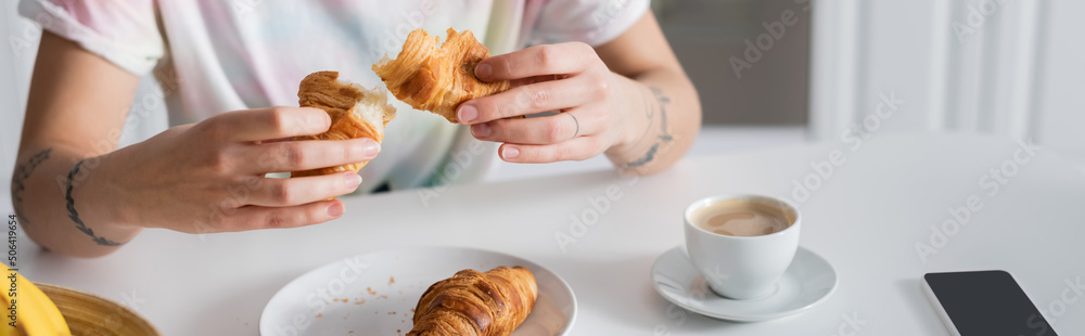 partial view of woman holding delicious croissant near coffee cup, banner