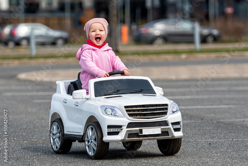 little girl drives a big white childrens electric toy car in the parking lot at the residential home photo