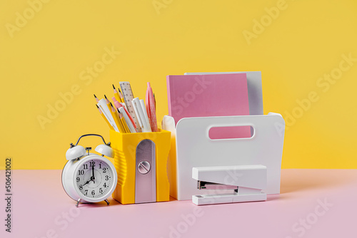 Fotografie, Obraz Yellow pencil holder and alarm with school stationery supplies on pink yellow background