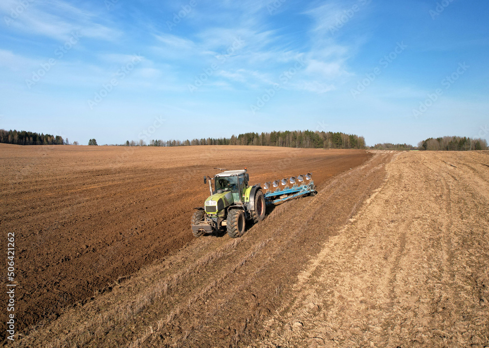 Tractor with plow on soil cultivating. Green tractor plowing field, drone view. Cultivated land and soil tillage. Agricultural tractor on field cultivation. Tractor disk harrow on plowing farm field. Tractor with plow on soil cultivating. Green tractor plowing field, drone view. Cultivated land and soil tillage. Agricultural tractor on field cultivation. Tractor disk harrow on plowing farm field.