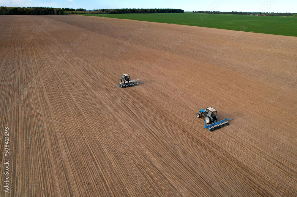 Tractor sowing seed on plowed field. Sowing seeds of corn and sunflower. Blue Tractor with disk harrow on plowing field. Seeding machinery on farm field. Seed sowing in farmland, aerial view..