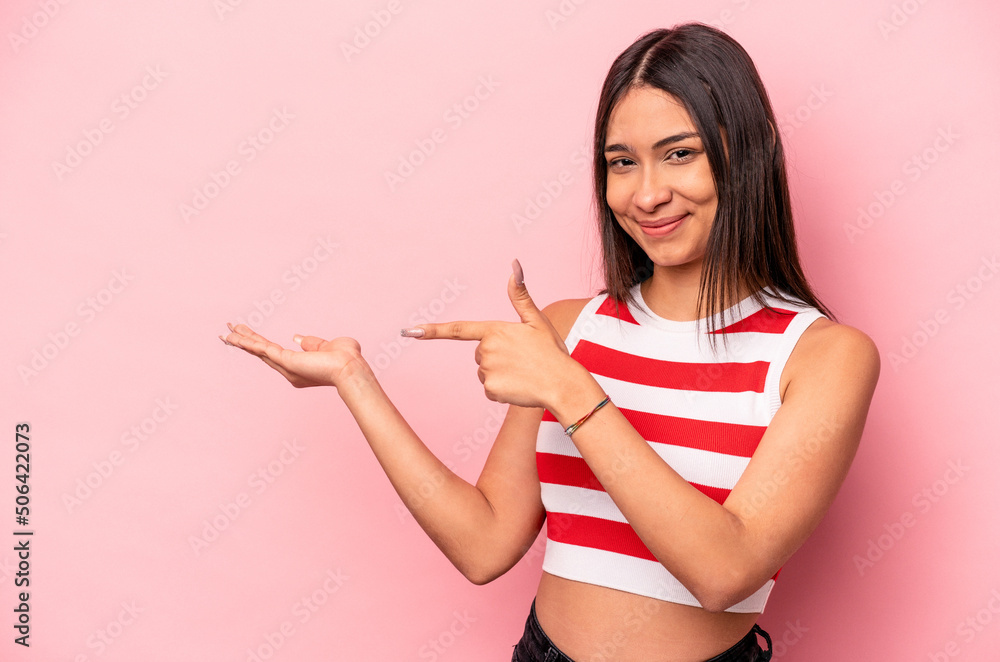 Young hispanic woman isolated on pink background excited holding a copy space on palm. Young hispanic woman isolated on pink background excited holding a copy space on palm.