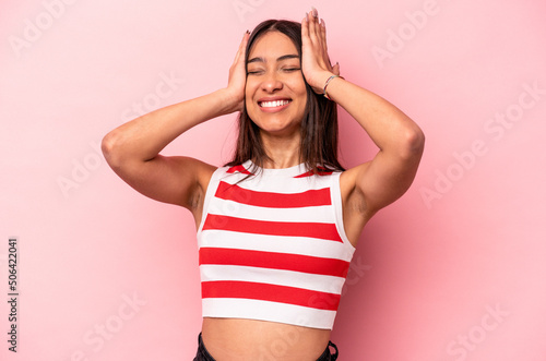 Young hispanic woman isolated on pink background laughs joyfully keeping hands on head. Happiness concept.