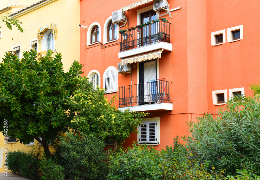 Naklejka premium House with palm trees and flowers in yard. Colorful facade and door of the house with apartments at Port Saplaya. Landscape design at suburb home. Garden with flowers near house on street courtyard..