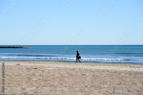 Girl is walking near the sea. Young woman walks along the sand of a beach near Mediterranean Sea against backdrop of waves and a stormy sky at sunset. Female person walks along coastline of the ocean.