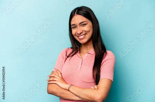 Young hispanic woman isolated on blue background who feels confident, crossing arms with determination.