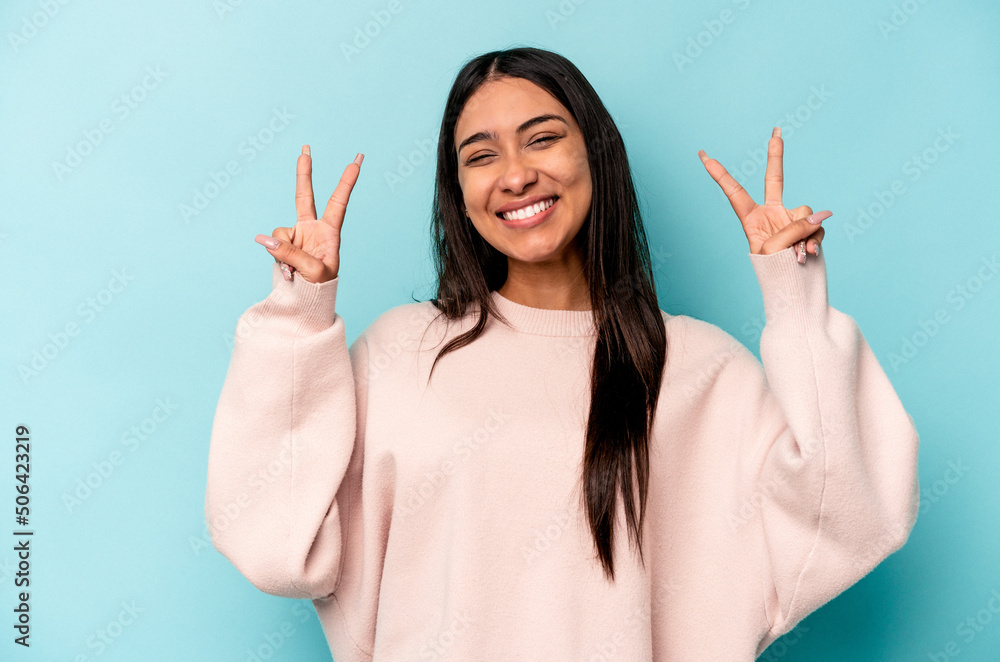 Young hispanic woman isolated on blue background showing victory sign and smiling broadly. Young hispanic woman isolated on blue background showing victory sign and smiling broadly.