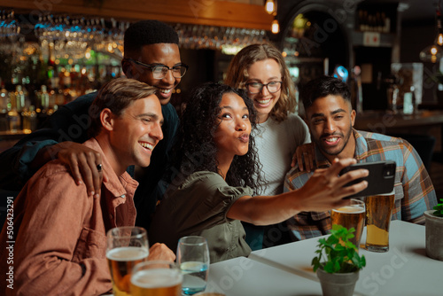 Mixed group of young adults sitting in restaurant taking selfies with cellular device