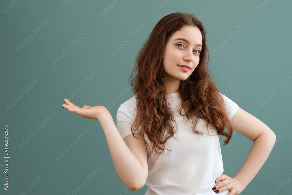 Teenage girl with blue eyes in white t-shirt is holding her palm up on teal background. Copy space, place for advertisement. Teenage girl with blue eyes in white t-shirt is holding her palm up on teal background. Copy space, place for advertisement.