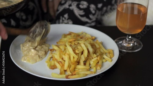 A person serving creamy sauce with a basting spoon on a plate with French fries, close up static photo