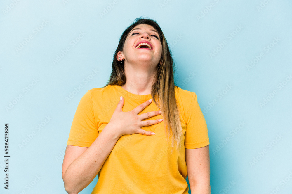 Young caucasian woman isolated on blue background laughs out loudly keeping hand on chest. Young caucasian woman isolated on blue background laughs out loudly keeping hand on chest.
