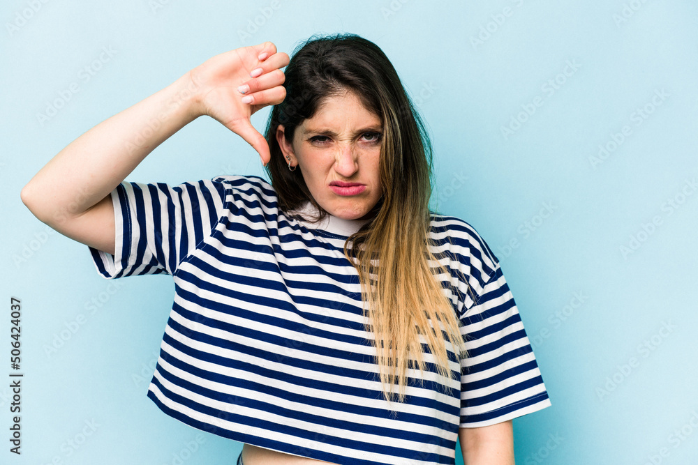 Young caucasian woman isolated on blue background showing thumb down and expressing dislike. Young caucasian woman isolated on blue background showing thumb down and expressing dislike.