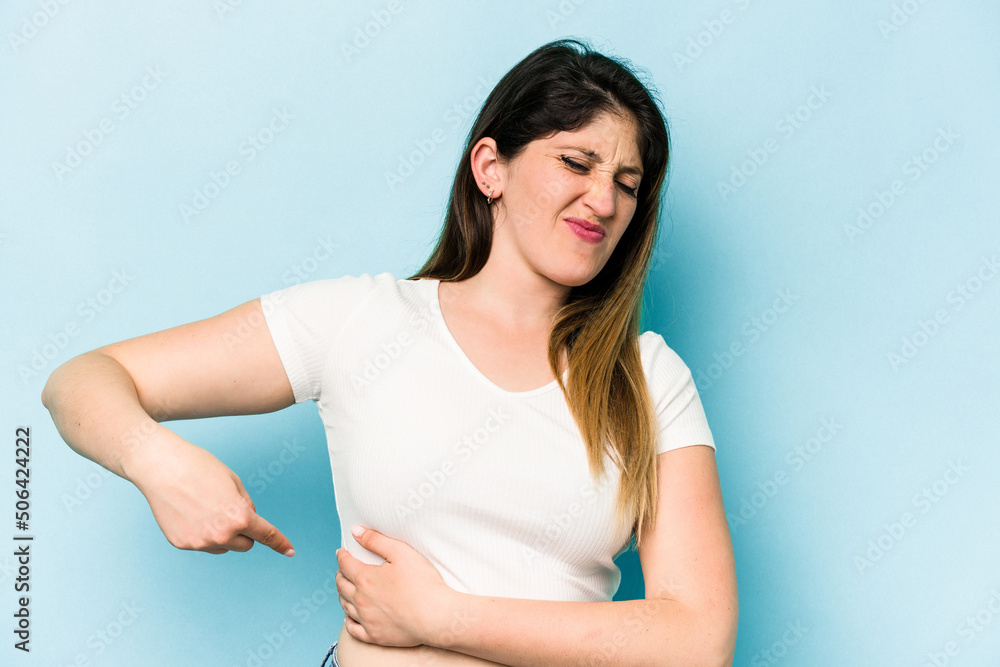 Young caucasian woman isolated on blue background having a liver pain, stomach ache. Young caucasian woman isolated on blue background having a liver pain, stomach ache.