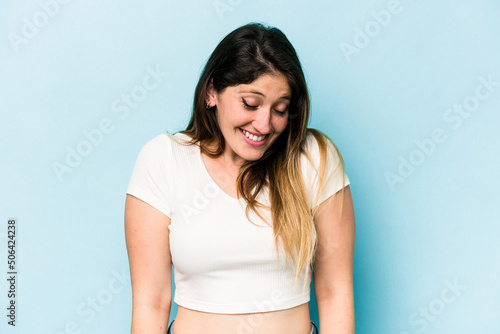 Young caucasian woman isolated on blue background laughs and closes eyes, feels relaxed and happy.