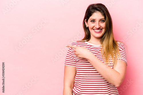 Young caucasian woman isolated on pink background smiling and pointing aside, showing something at blank space.