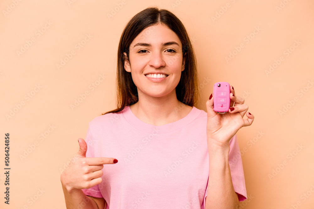 Young hispanic woman holding a keys car isolated on beige background person pointing by hand to a shirt copy space, proud and confident Young hispanic woman holding a keys car isolated on beige background person pointing by hand to a shirt copy space, proud and confident