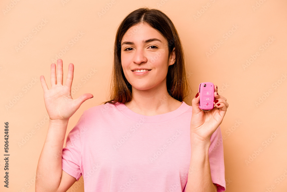 Young hispanic woman holding a keys car isolated on beige background smiling cheerful showing number five with fingers. Young hispanic woman holding a keys car isolated on beige background smiling cheerful showing number five with fingers.