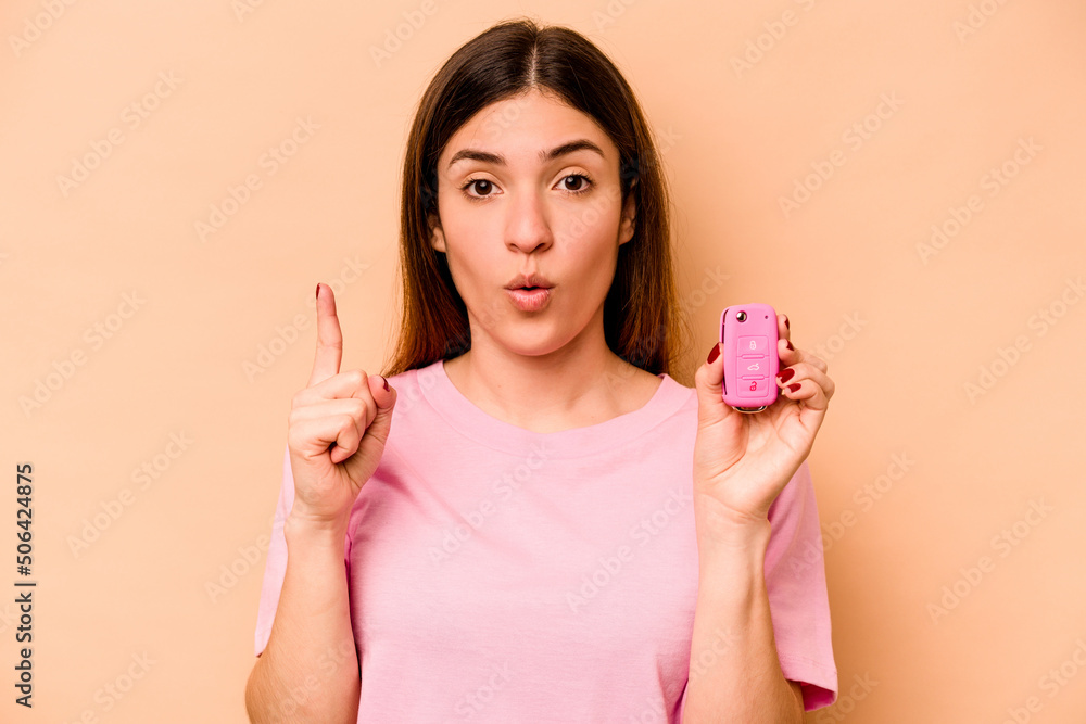 Young hispanic woman holding a keys car isolated on beige background having some great idea, concept of creativity. Young hispanic woman holding a keys car isolated on beige background having some great idea, concept of creativity.