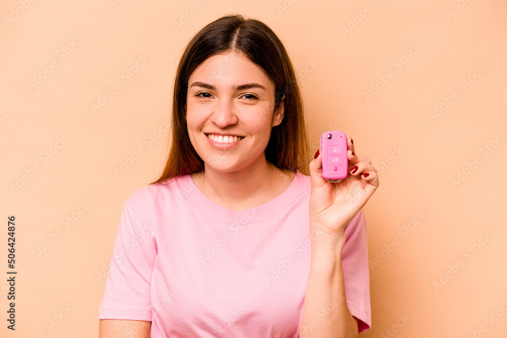 Young hispanic woman holding a keys car isolated on beige background laughing and having fun. Young hispanic woman holding a keys car isolated on beige background laughing and having fun.