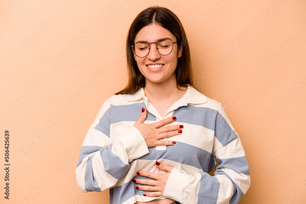 Young hispanic woman isolated on beige background laughs happily and has fun keeping hands on stomach. Young hispanic woman isolated on beige background laughs happily and has fun keeping hands on stomach.