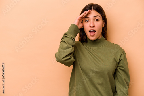 Young hispanic woman isolated on beige background shouts loud, keeps eyes opened and hands tense. © Asier