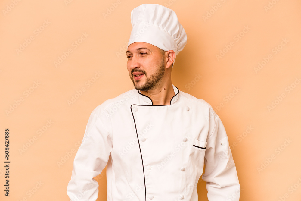 Hispanic chef man isolated on beige background looks aside smiling, cheerful and pleasant. Hispanic chef man isolated on beige background looks aside smiling, cheerful and pleasant.