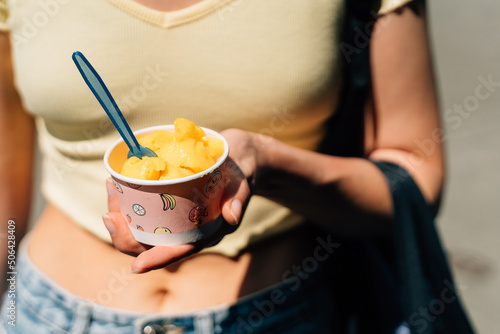 Close up of teen girl with paper cup with mango yellow sorbet ice cream on sunny summer day photo