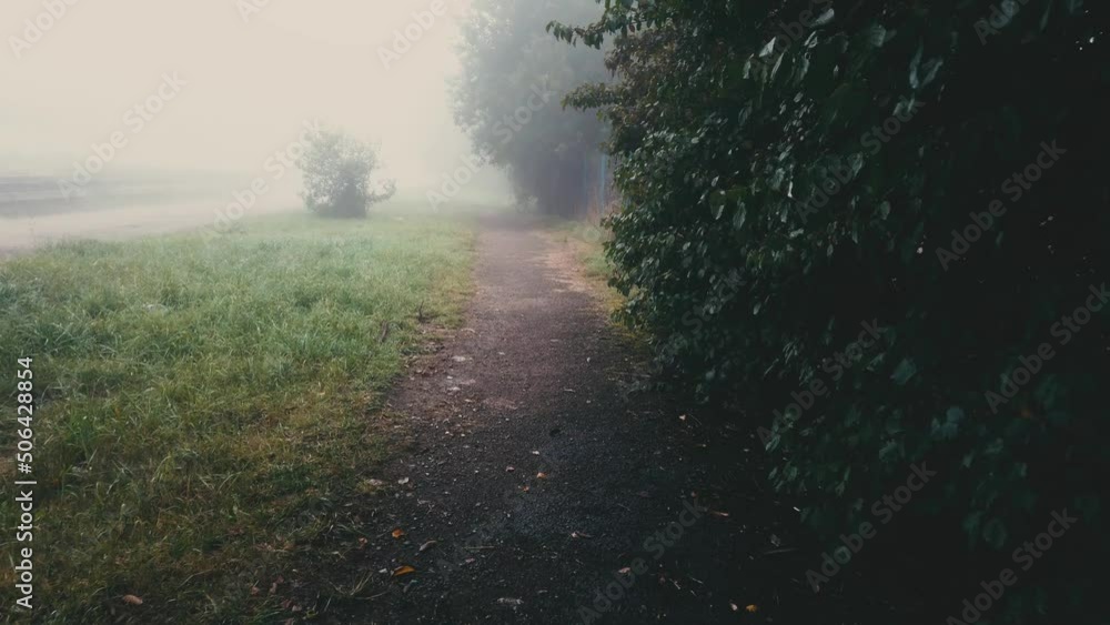 Walking on sidewalk in fog and falling rain. Misty autumn landscape and footpath at dusk. Motion on foggy street Walking on sidewalk in fog and falling rain. Misty autumn landscape and footpath at dusk. Motion on foggy street