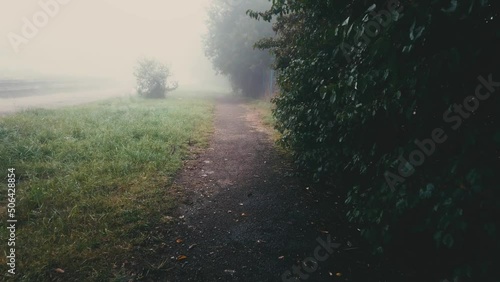 Walking on sidewalk in fog and falling rain. Misty autumn landscape and footpath at dusk. Motion on foggy street