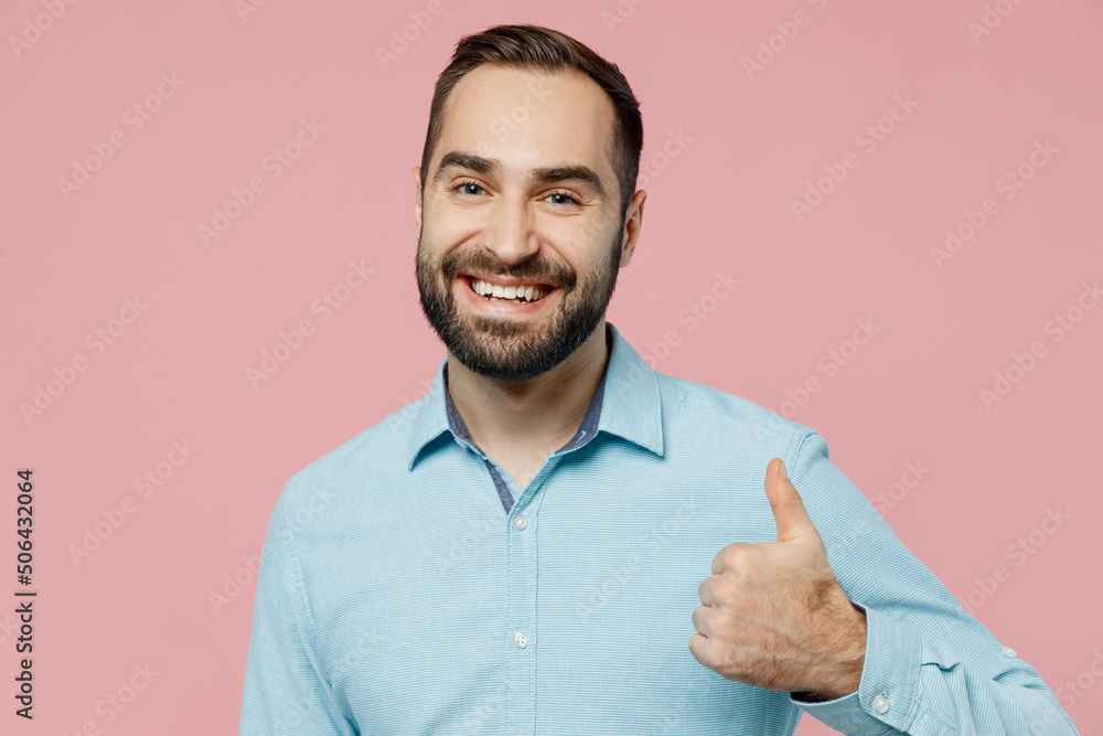 Young smiling satisfied happy fun cool caucasian man 20s wear classic blue shirt showing thumb up like gesture isolated on plain pastel light pink background studio portrait. People lifestyle concept. Young smiling satisfied happy fun cool caucasian man 20s wear classic blue shirt showing thumb up like gesture isolated on plain pastel light pink background studio portrait. People lifestyle concept.