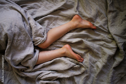 Legs laying in bed with grey sheets photo