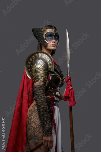 Studio shot of tattooed ancient amazon dressed in armor and red cloak holding spear Fototapet