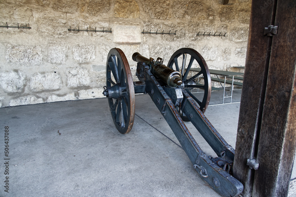 shooting cannon with wheels from the middle ages in front of a white stone wall, object ideal for freeing for photo compositions, black-brown metal, in the day, photographed from behind left shooting cannon with wheels from the middle ages in front of a white stone wall, object ideal for freeing for photo compositions, black-brown metal, in the day, photographed from behind left