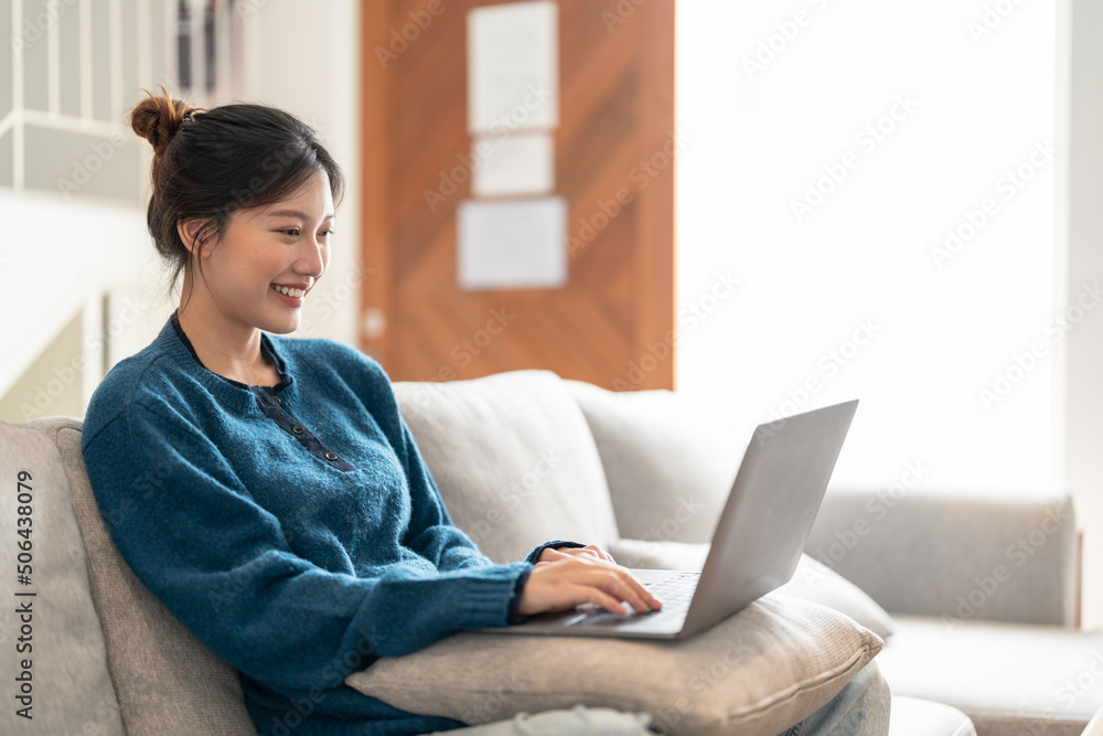 Smiling young asian woman using laptop, sitting on couch at home Smiling young asian woman using laptop, sitting on couch at home
