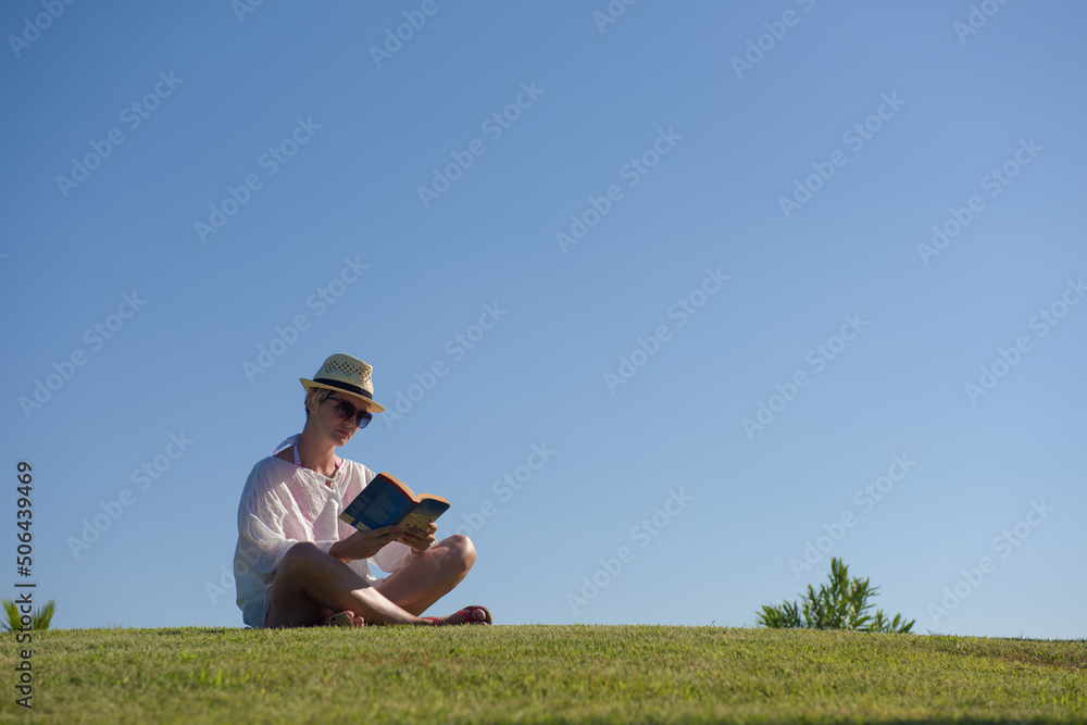Woman lying and reading her favorite book on a meadow covered with fresh green grass on a sunny summer or spring day. Woman lying and reading her favorite book on a meadow covered with fresh green grass on a sunny summer or spring day.