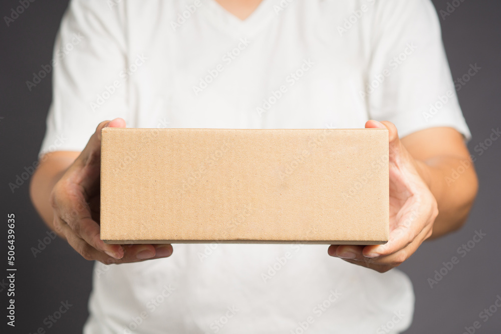 Man in white casual holding a cardboard box while standing on a gray background Man in white casual holding a cardboard box while standing on a gray background